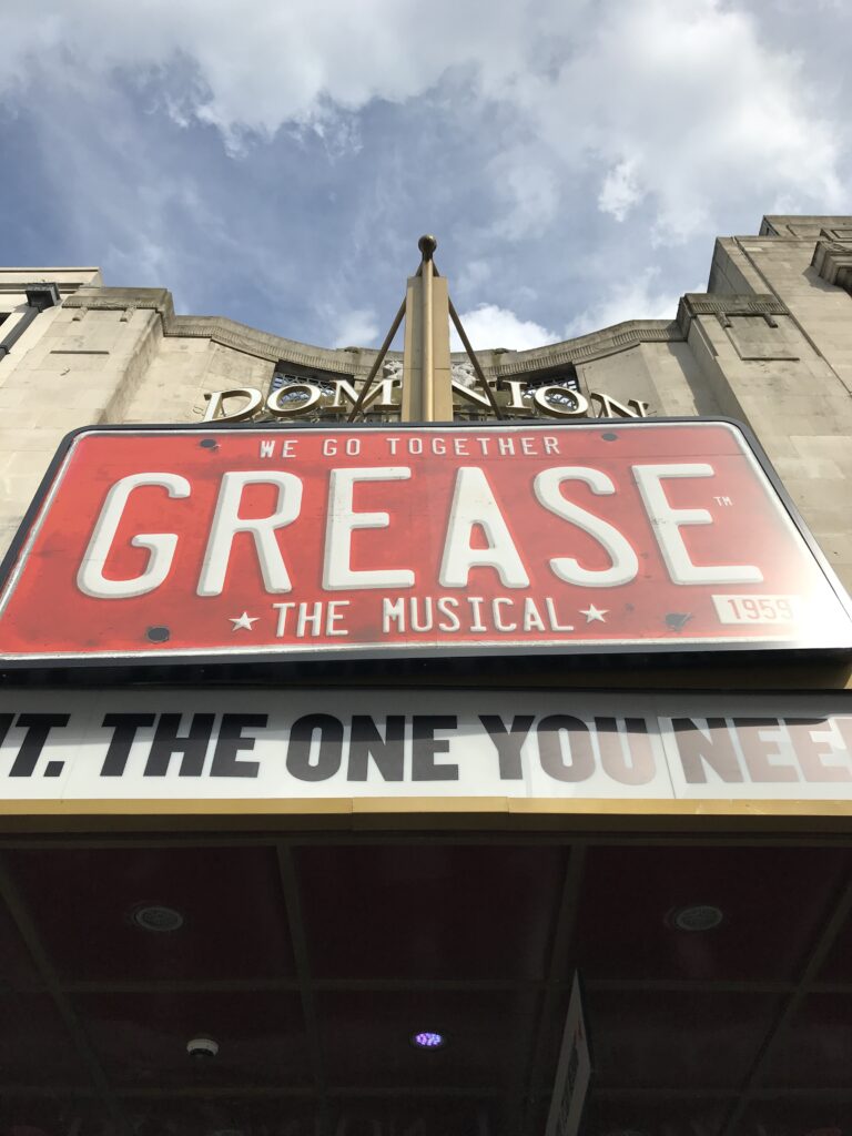 Grease the musical signage outside the dominion theatre. amyleighchandler reviews this hit musical and explores whether this iconic storyline is still appropriate in today's society. The review includes analysis of the set design and costumes as well as what the show could do better.